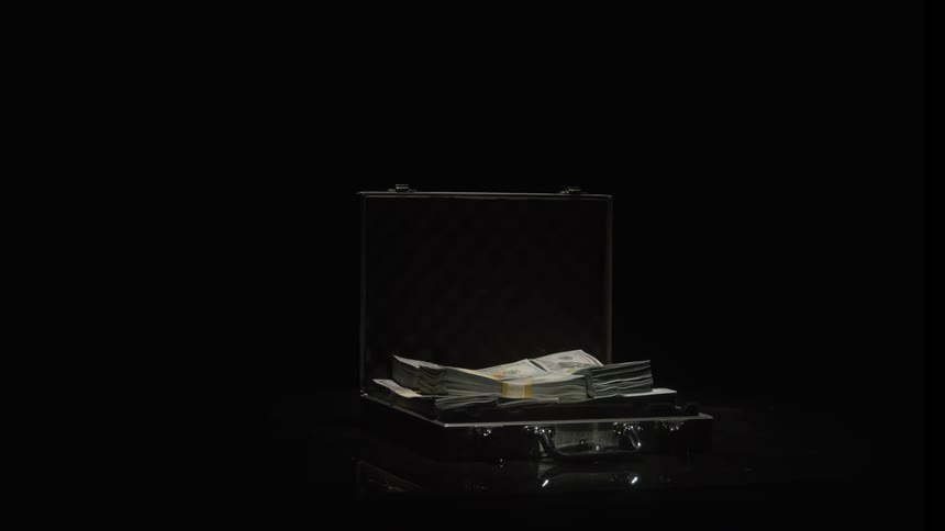 A briefcase full of money rests in a dark spotlight