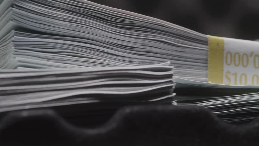 The video features a closeup view of numerous tightly packed stacks of us dollar bills likely 100 denominations with some bundles clearly marked with a 10000 yellow band the stacks are seen moving through what appears to be a money counting