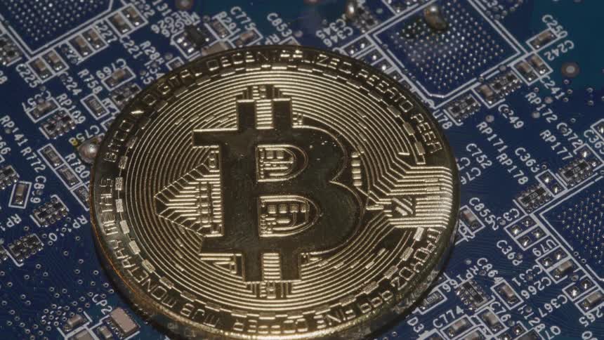 A closeup rotating shot captures a physical gold bitcoin resting on a complex blue computer circuit board