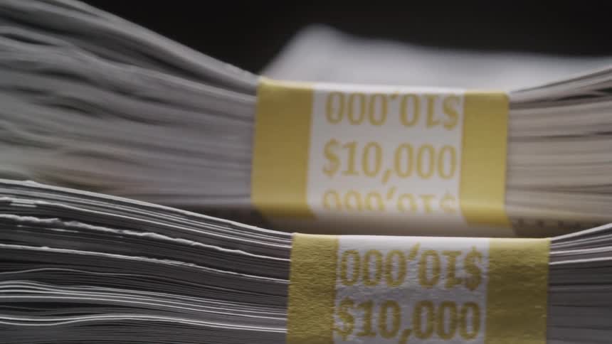 A closeup shot pans across multiple thick stacks of cash each bound by a yellow and white 10000 currency strap