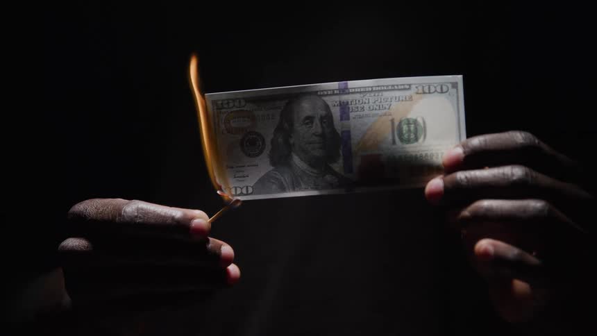 Black hands setting paper money on fire with a match