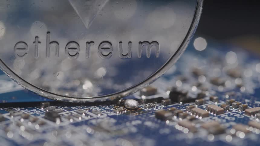 A shiny and reflective coin is upright on its edge atop a circuit board
