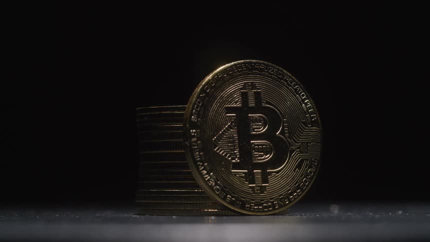 A coin with the bitcoin logo imprinted upon it is propped against a stack of coins