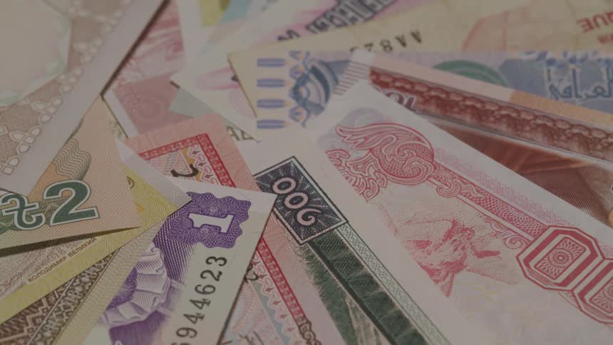 Multiple bills of different currencies are piled atop each other
