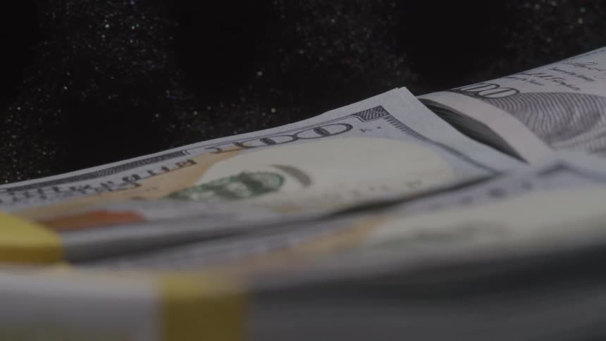 The camera pans around a stack of one hundred dollar bills