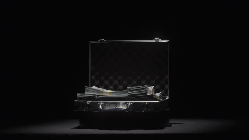 A briefcase full of cash is dramatically lit in a dark minimal setting