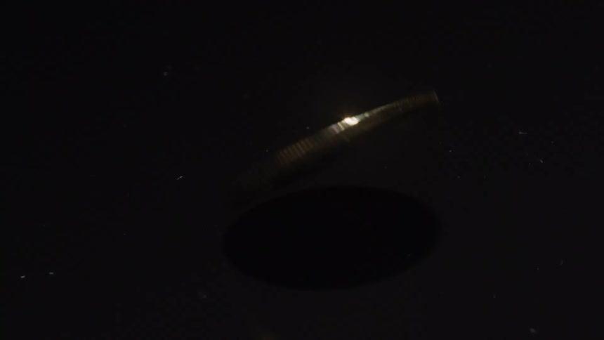 A shiny golden colored coin spins on a reflective surface