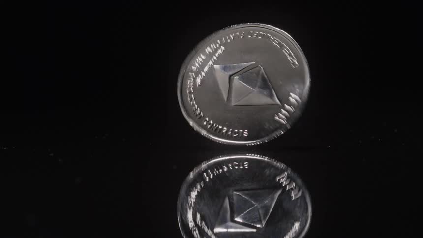 A silver ethereum coin spins on a glossy black surface with a clear reflection