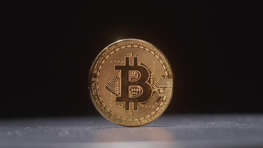 A golden coin with the bitcoin logo is balanced upright on its edge