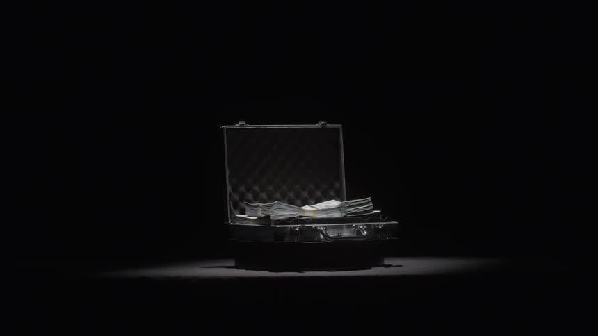 A metallic briefcase sits in a dark spotlit room slowly opening to reveal stacks of cash illuminated by the beam of light the scene dramatically highlights the reveal of a large sum of money emphasizing themes of secrecy or illicit dealings