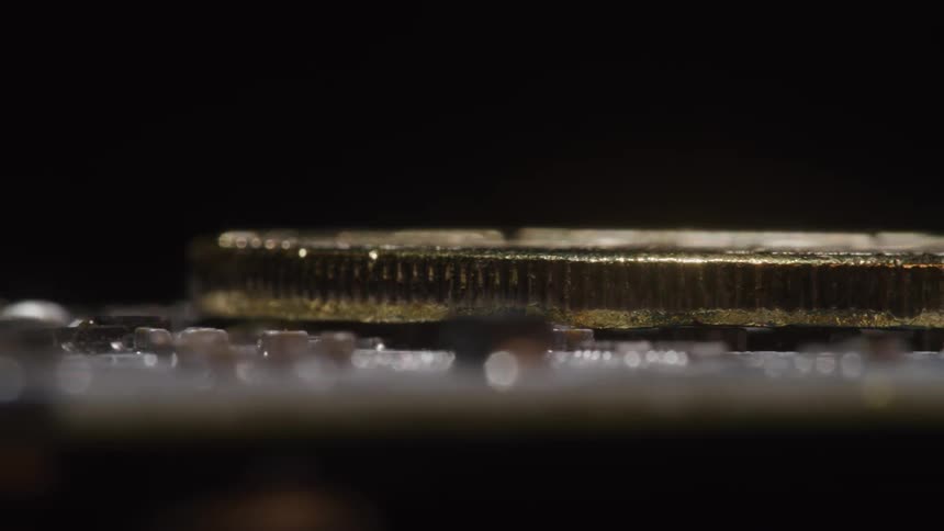 An extreme closeup shot pans across a physical gold bitcoin resting on a computer circuit board