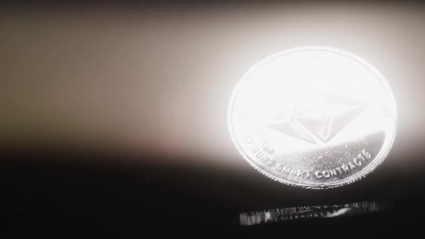 A silver ethereum cryptocurrency coin spins continuously in a dark room