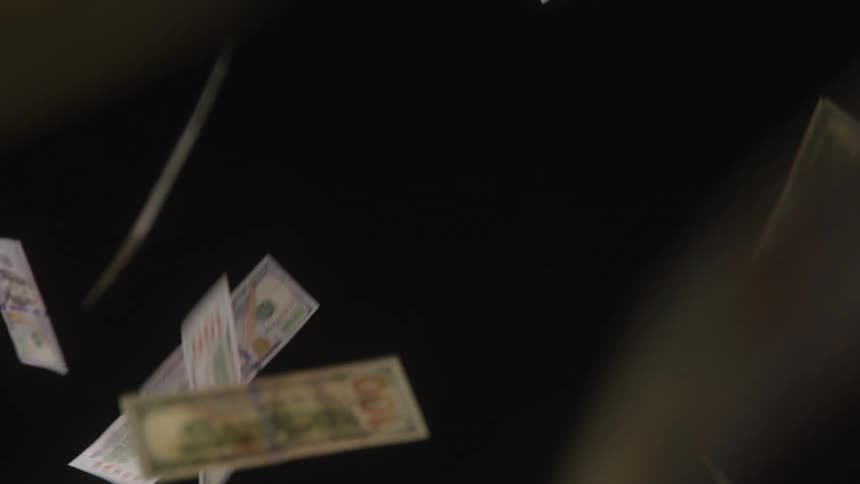 Multiple paper dollar bills fall slowly downward through the air