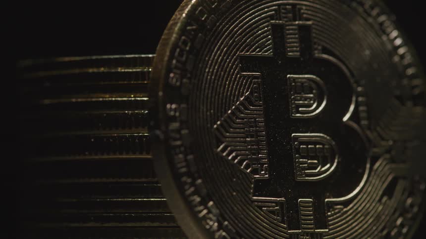 Close up of a physical bitcoin placed vertically beside a stack of similar coins on a rotating surface in a dark room