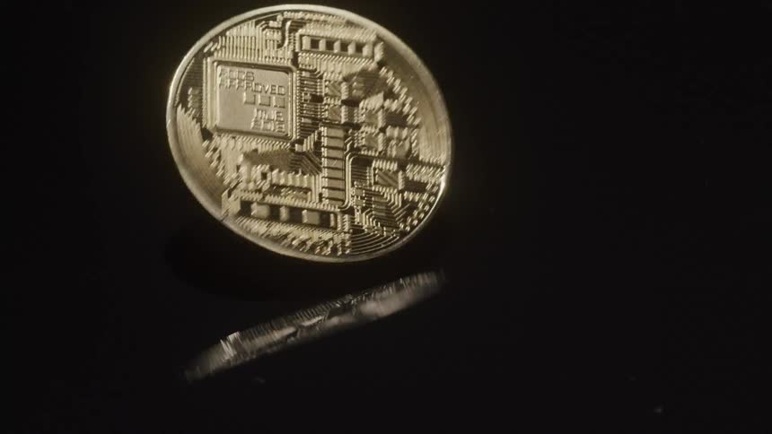 A reflective gold coin is turning on a black background