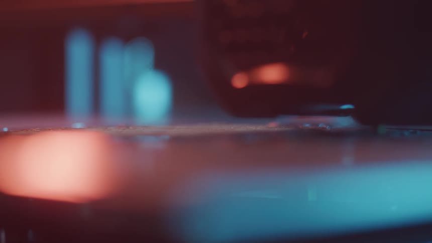 An abstract extreme closeup shows a 3d printer nozzle working illuminated by moody red and blue lights with a shallow depth of field