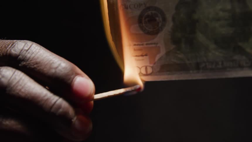 A person uses a match to burn money