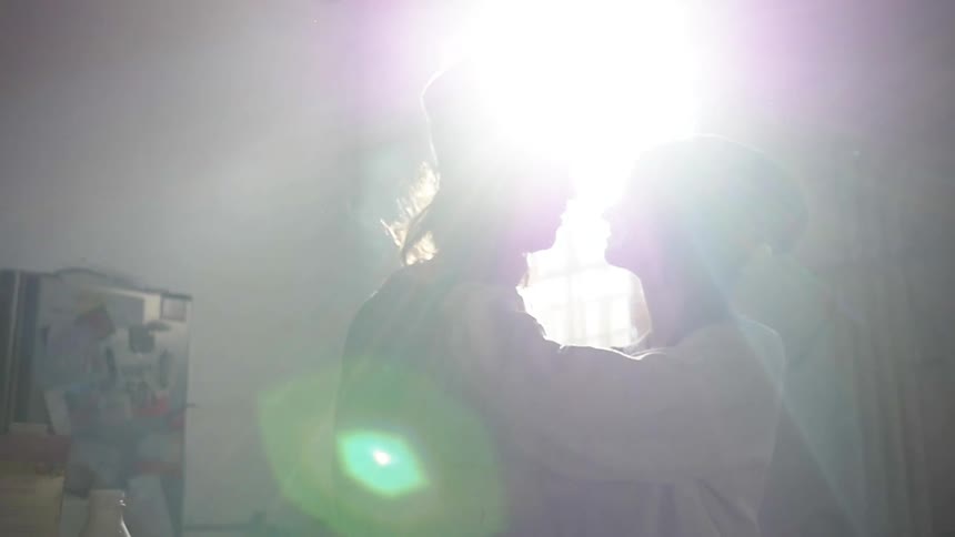 A man and woman kiss in front of a sunlit window