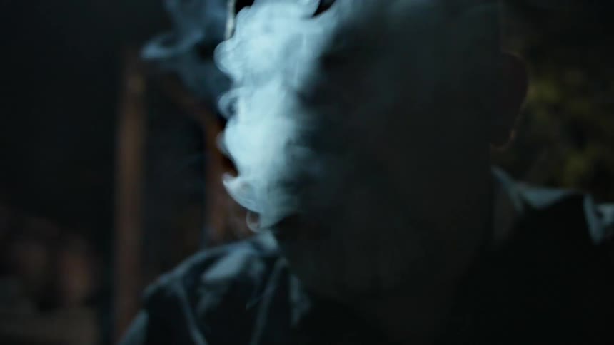 A man smokes a cigar in a dark room