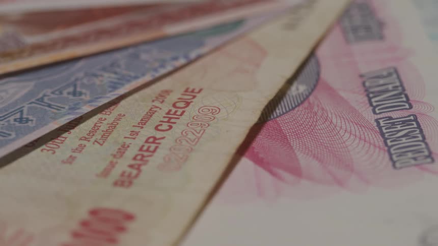 A collection of various international banknotes including the vietnamese zimbabwean currency and dinar laid out side by side the camera slowly pans across the different denominations and designs