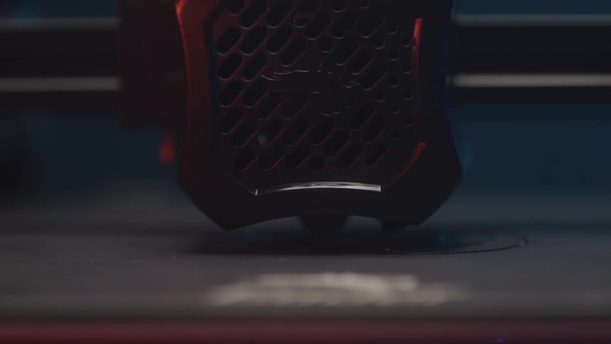 A closeup shot shows a 3d printers nozzle moving as it applies a layer of material to a surface