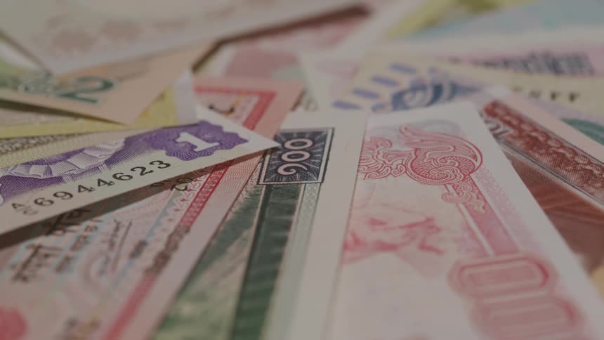 Multiple paper bills of various currencies are arranged atop each other