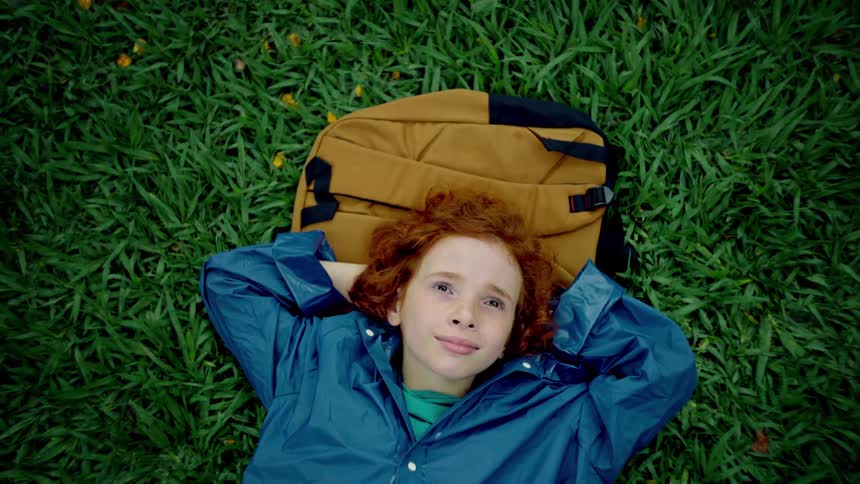 A child looks up at the sky while laying on the grass