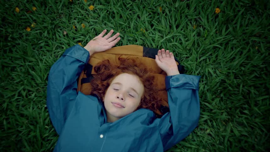 A child with curly red hair lies peacefully on the grass with eyes wide