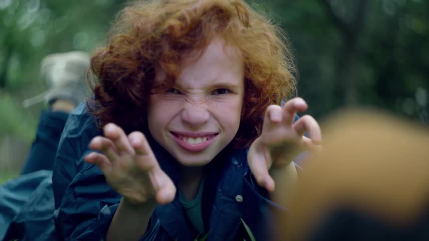 A young girl with curly red hair makes a silly face at the camera