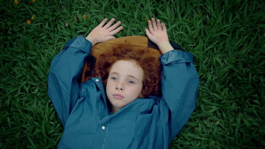 A child lays down on a backpack in the grass