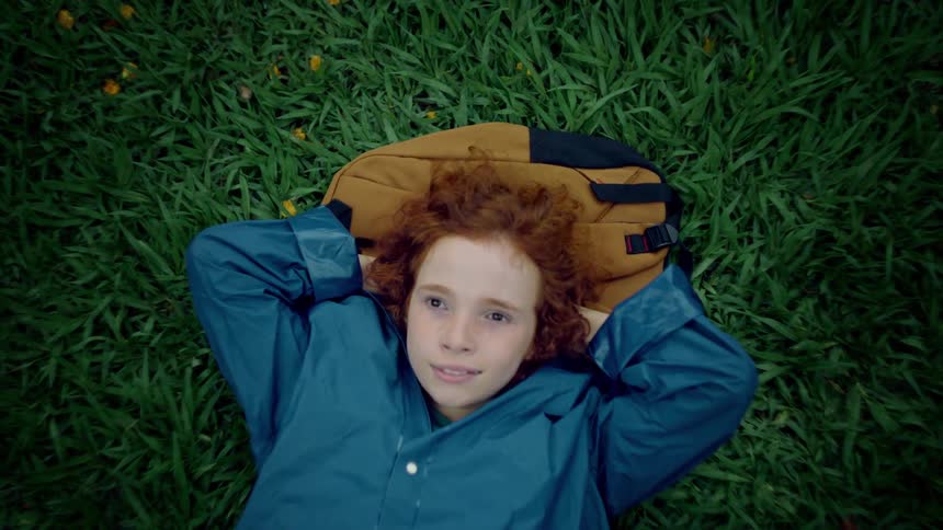A boy lays down and puts his head on the backpack