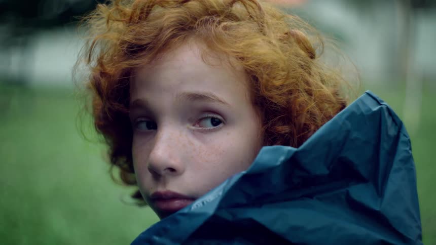 Redheaded youth wearing a rain coat looks over her shoulder