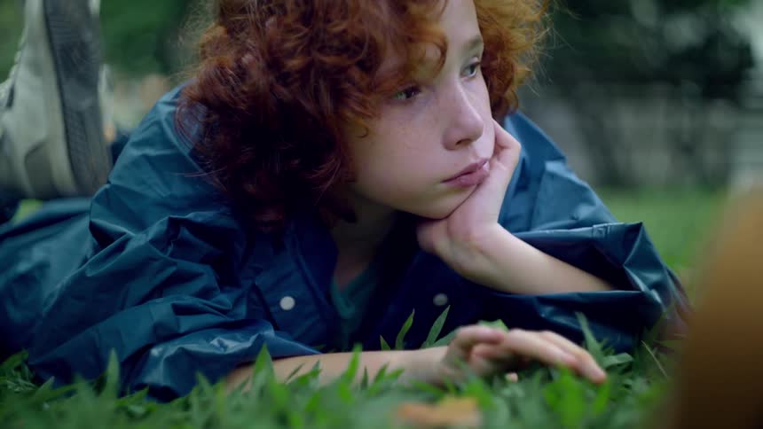 The boy touches the grass while laying down