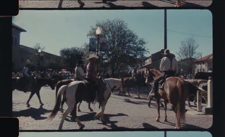 A group of cowboys on horseback rides through a town street on a bright sunny day the video has a vintage filmlike aesthetic with rounded corners giving it a nostalgic feel