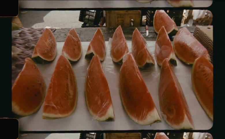 Several slices of watermelon arranged in rows on a table at an outdoor market