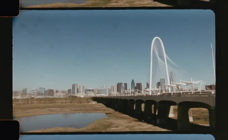 The margaret hunt hill bridge stands prominently against the dallas city skyline on a clear sunny day