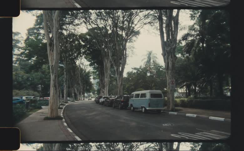 Blue van parked behind line of cars on a tree lined road