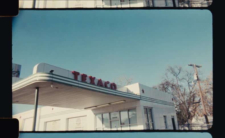 An archival film shot shows a vintage texaco gas station with its classic red logo against a clear blue sky