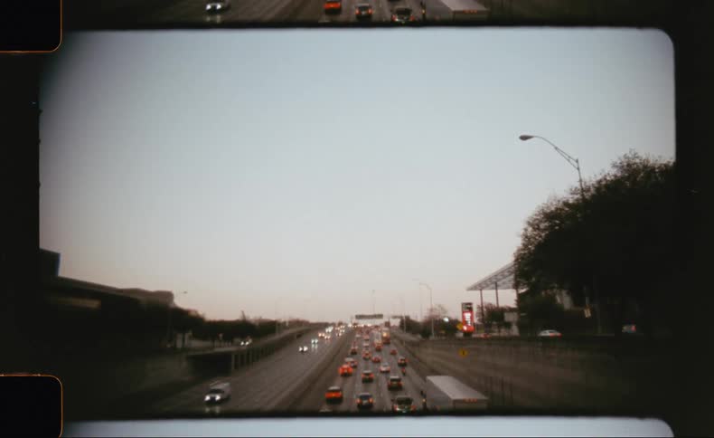The video displays a wide view of a multilane highway from a moving vehicle with traffic flowing in both directions the scene framed to resemble a film reel with rounded corners captures a grey possibly overcast day