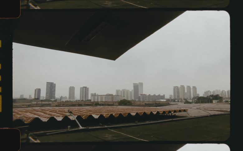 A wide archival style city shot showing distant highrise buildings framed from a dark interior