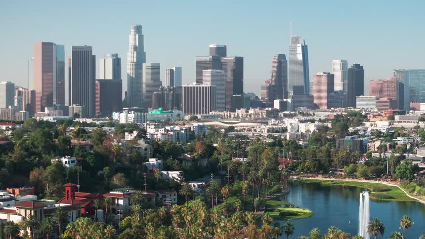 Water spouts Echo Park Lake surrounded by residential buildings while a light haze covers nearby downtown Los Angeles skyline