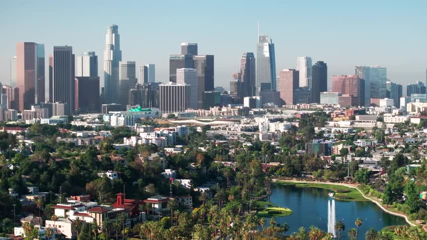 Downtown los angeles skyline stretches beyond echo park lake framed by palm trees and densely packed neighborhoods under a hazy sky
