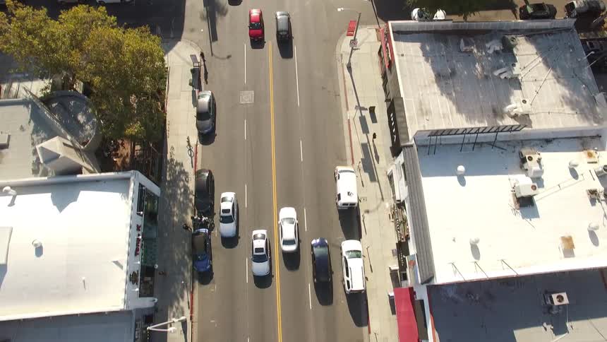 A congested multilane intersection funnels traffic past palmlined sidewalks storefronts and parked cars under afternoon light