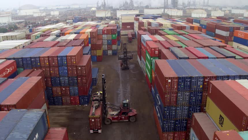 An expansive aerial view of a shipping yard filled with numerous colorful cargo containers stacked high in the middle of the yard several large forklifts or reach stackers are seen moving containers indicating active operations at the facility