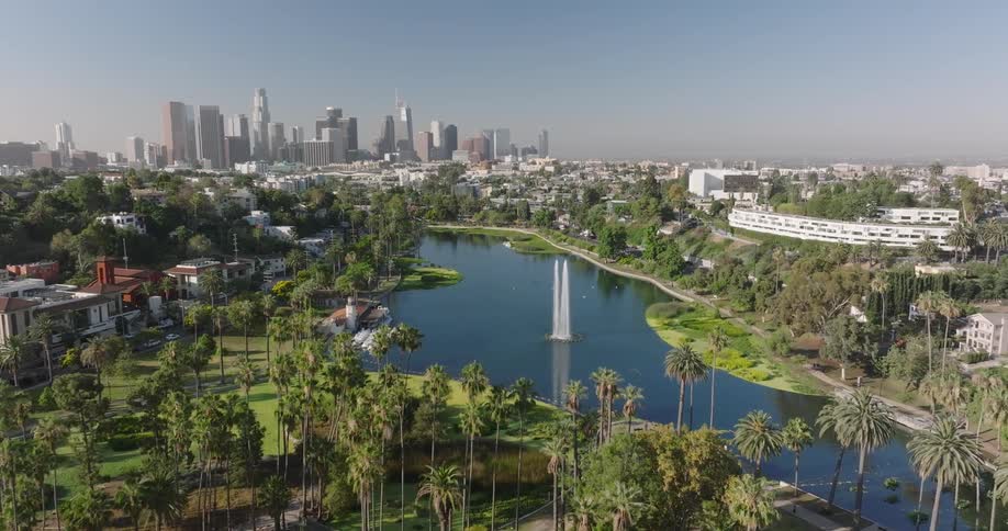 Aerial view of echo park lake in los angeles california showcasing its vibrant green surroundings and the iconic fountain in the center of the water in the background the distinctive skyline of downtown los angeles rises offering a striking contrast