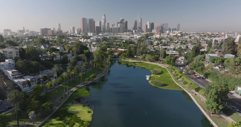 Traffic passes the park surrounding a lake in the residential area of a large city on a summer day