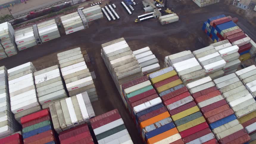 Vast rows of colorful shipping containers are stacked high across a sprawling industrial yard
