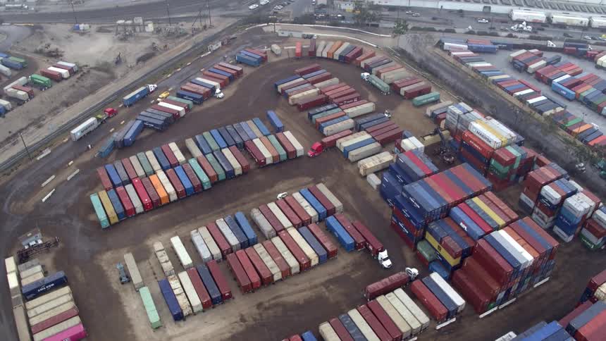 A seaport filled with shipping containers with trucks bringing in more containers at midday