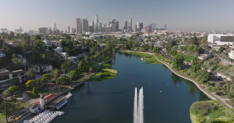 A calm Echo Park Lake in Los Angeles reflects trees and city buildings under a clear sky