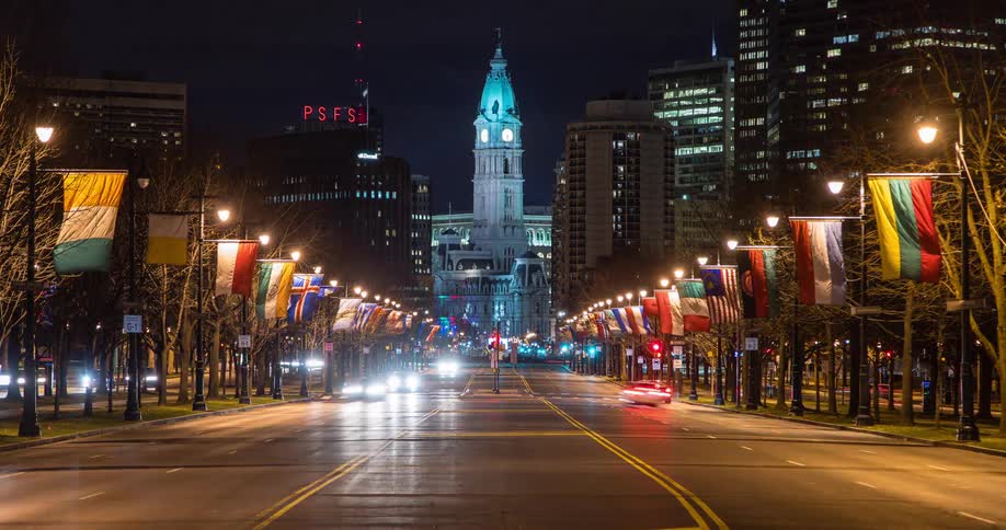 Traffic flowing in both directions on a busy Philadelphia street with flags lining both sides